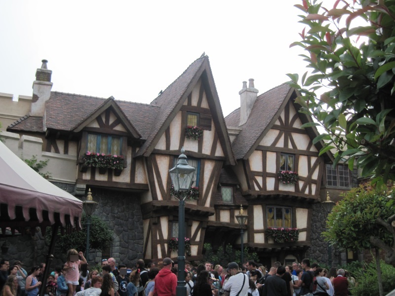 Fairy-tale architecture in Fantasyland, Disneyland Park, Paris, and people waiting in line to join a roller-coaster ride.