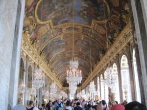 Versailles Palace's Hall of Mirrors abounds with colorful frescoes, opulent chandeliers, elaborate sculptures, and visitors.