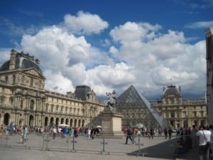 Visitors to Louvre Museum can see a glass pyramid in the courtyard and the elaborate architecture of a former royal palace.