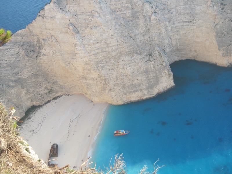 Photographed from above, Navagio Beach on Zakynthos Island, Greece, reveals steep cliffs, a shipwreck, and turquoise waters.