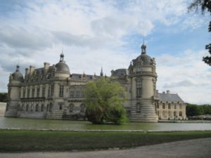 View of Château de Chantilly in Picardy in a cloudy setting with lawn and canal in front of the Renaissance palace.