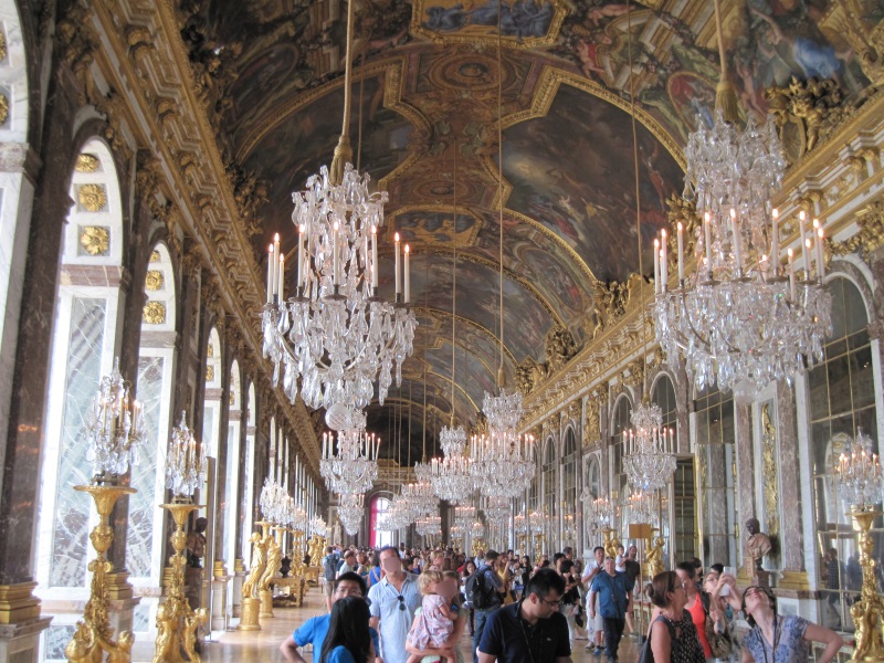 Versailles Palace's Hall of Mirrors teems with frescoes, chandeliers, mirrors, and visitors examining its matchless splendor.