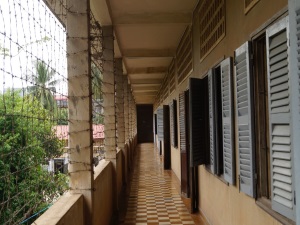 The Tuol Sleng Genocide Museum's corridor features wires to the left and prison cells' doors and windows to the right.
