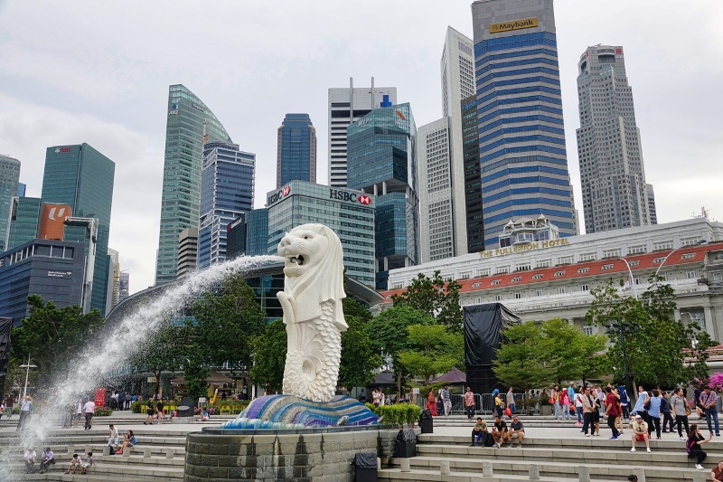 Merlion, half-lion, half-fish creature, spouts water from its mouth while Singapore skyscrapers stand in the background.