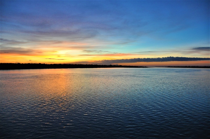 The calm surface of Tonle Sap Lake near Siem Reap, Cambodia, during sunset, with distant clouds and blue and orange sky.