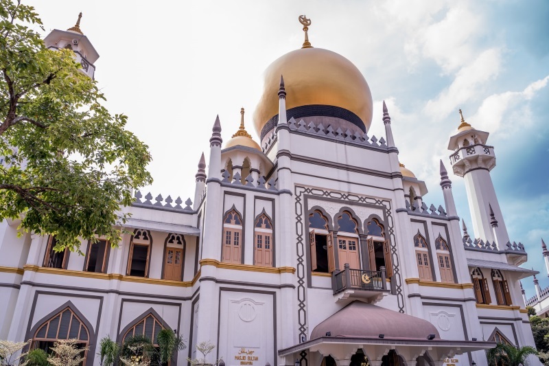 Sultan Mosque, Singapore, boasts a large, golden dome, tall towers with gilded roofs, and a white facade with arched windows.